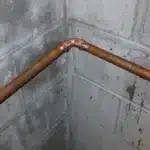 Copper pipes above red bucket in basement corner