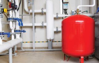 Industrial valves and a red pressure tank installed within a boiler system, showing the components of a boiler expansion tank setup. Image used for Cardom Plumbing & Heating’s guide on Boiler Expansion Tanks, highlighting system pressure management and essential plumbing hardware.