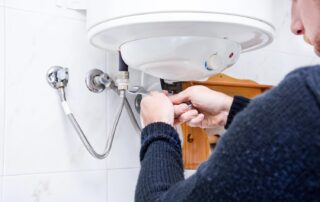 Cardom Plumbing and Heating fixes Common Water Heater Issues. A plumber repairs a water heater with a wrench to ensure efficient performance.