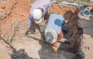 Two workers repairing an underground water pipe leak, using tools and safety gear as they uncover damaged plumbing. Scene illustrates how Colorado’s freeze-thaw cycles strain buried pipes, leading to cracks, leaks, and emergency repairs.