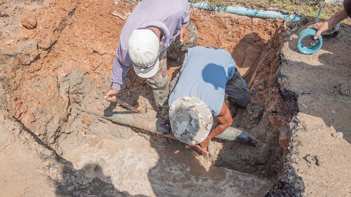 Two workers repairing an underground water pipe leak, using tools and safety gear as they uncover damaged plumbing. Scene illustrates how Colorado’s freeze-thaw cycles strain buried pipes, leading to cracks, leaks, and emergency repairs.
