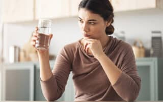 A woman inspects her glass, puzzled and concerned—I Have Black Specks in My Water. What Are They? Cardom Plumbing & Heating can help.