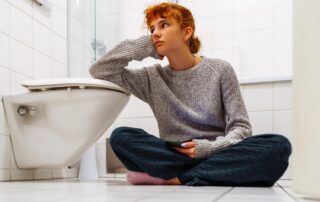 Person sitting on bathroom floor, looking thoughtful.