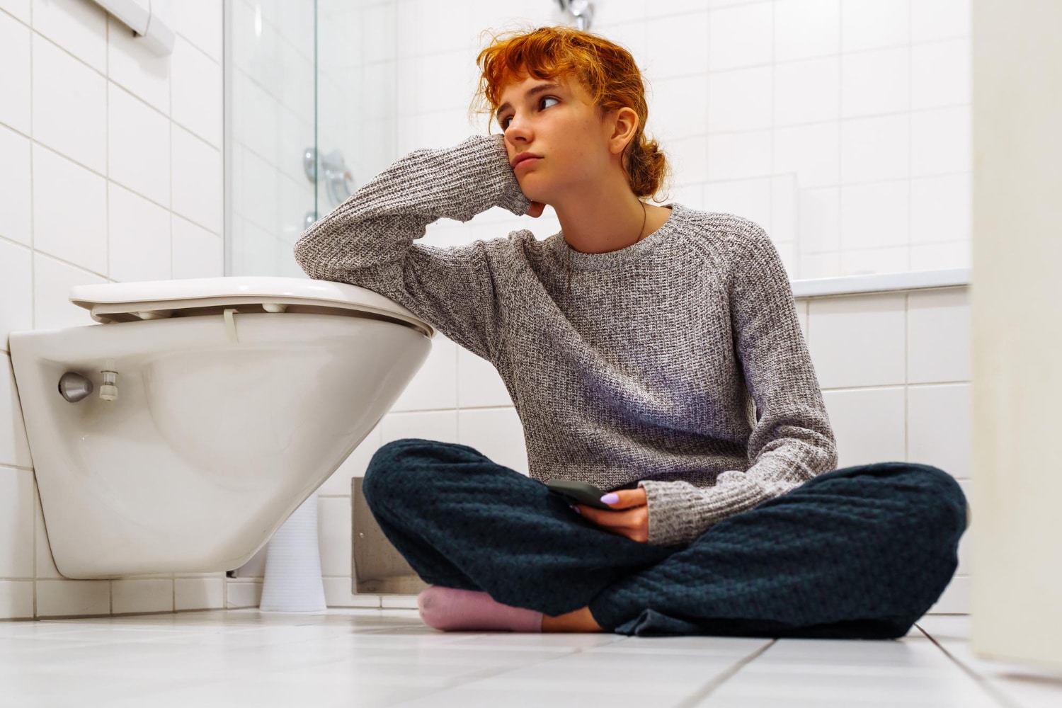 Person sitting on bathroom floor, looking thoughtful.