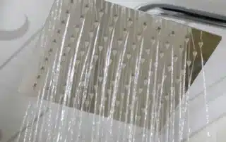 Shower goes cold when the washer runs, explaining cross demand conflicts in household plumbing, illustrated by water flowing from a square showerhead, and covering pressure balance valves, flow rates, and system upgrades to stabilize temperature.