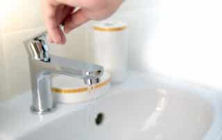 Hand turning on faucet with running water