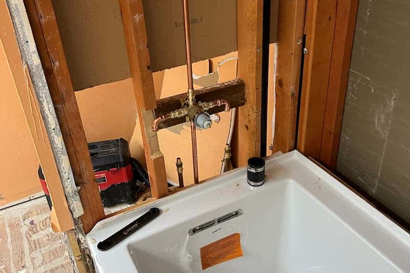 Bathtub installation in progress with exposed pipes.