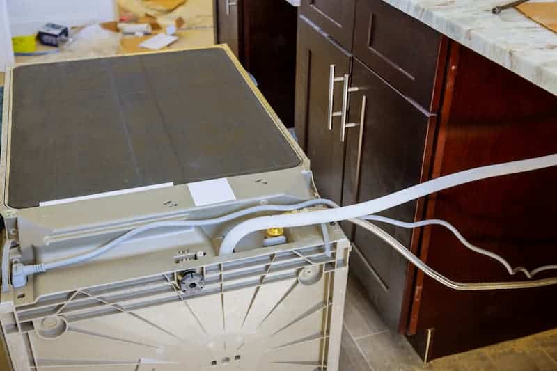 Installed dishwasher with visible plumbing connections in kitchen.