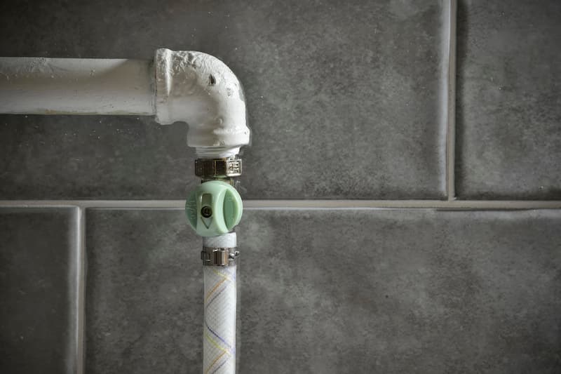 Pipe and valve against tiled wall background.